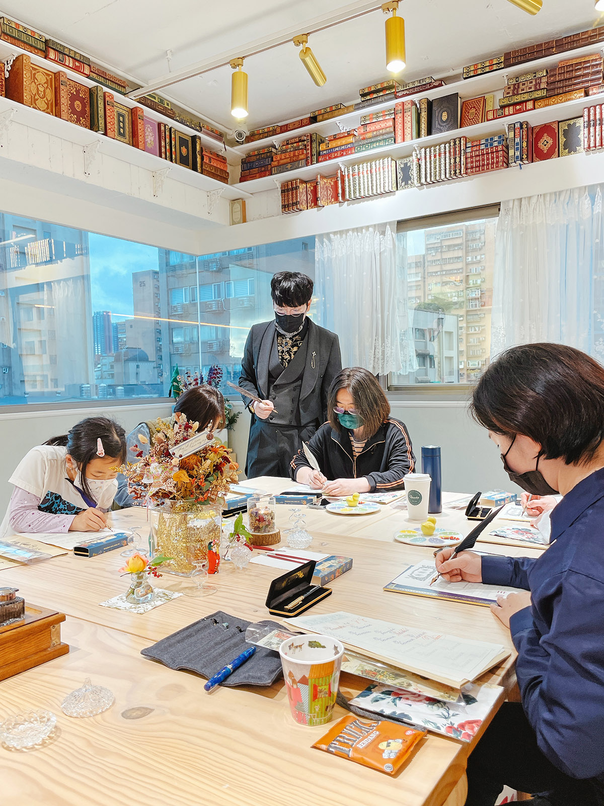日日好文創大安區實體小班課程現場，老師於古書環繞的教室中指導不同年齡學員進行鋼筆書寫與美字練習。