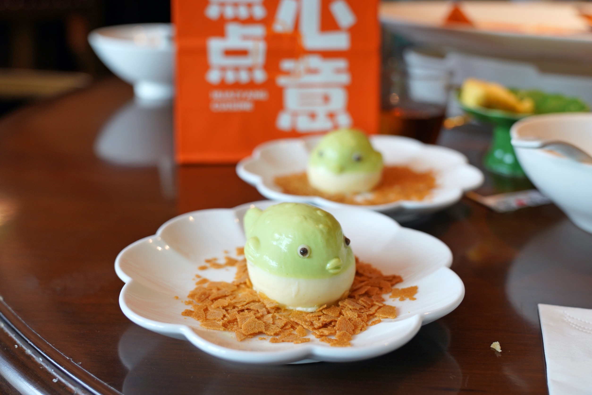 白色花形餐盤上的綠色小河豚造型慕斯甜點與餅乾碎片